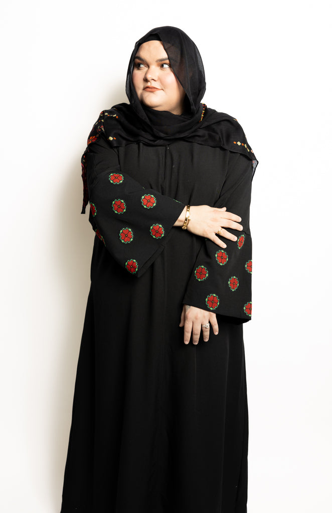 a black abaya with button clasps and pockets and watermelon and poppy tatreez palestinian embroidery along the sleeves