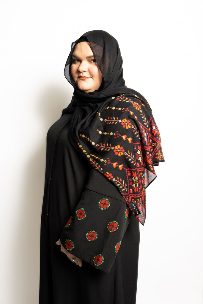 a black abaya with button clasps and pockets and watermelon and poppy tatreez palestinian embroidery along the sleeves