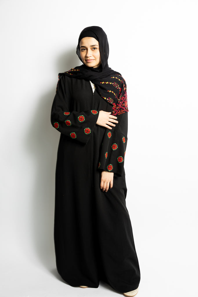 a black abaya with button clasps and pockets and watermelon and poppy tatreez palestinian embroidery along the sleeves