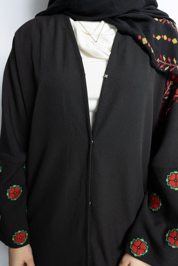 a black abaya with button clasps and pockets and watermelon and poppy tatreez palestinian embroidery along the sleeves