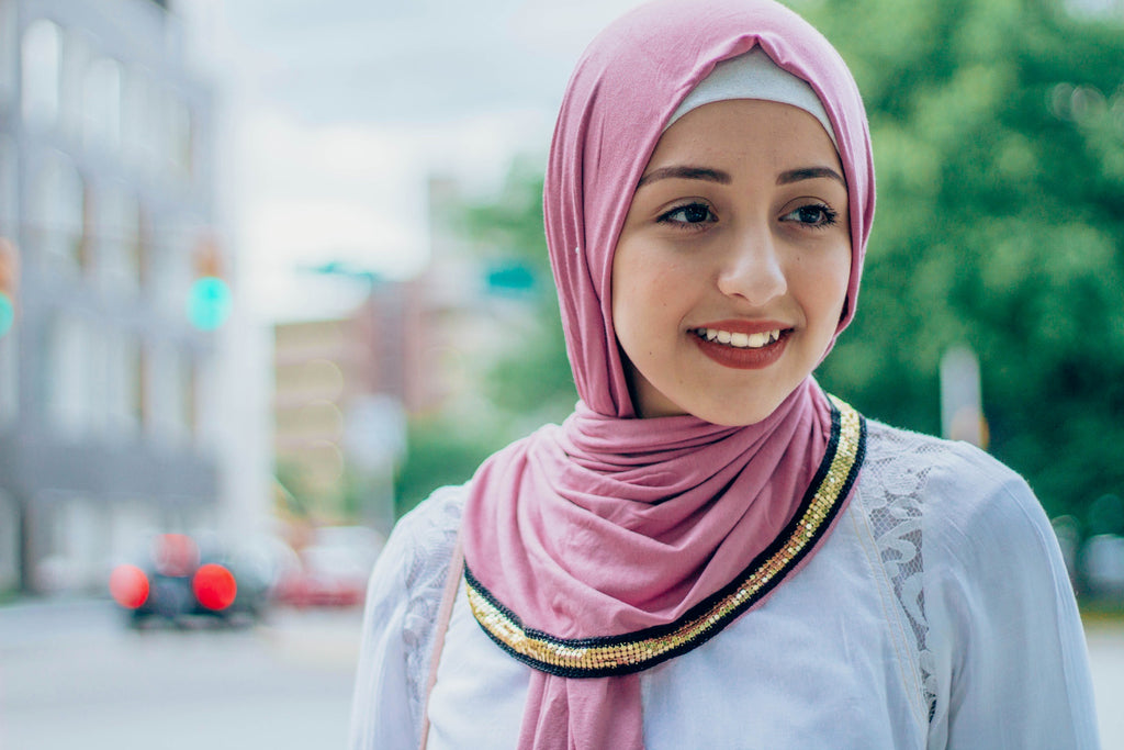 muslim woman wearing white top and white pants with a pink jersey hijab with a gold trim along the edges