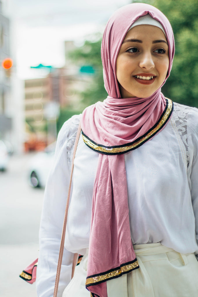 muslim woman wearing white top and white pants with a pink jersey hijab with a gold trim along the edges