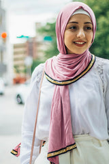 muslim woman wearing white top and white pants with a pink jersey hijab with a gold trim along the edges