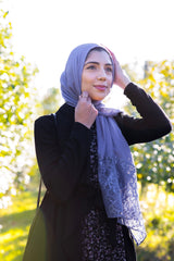 hijabi woman wearing a periwinkle purple modal hijab with lace ends wearing all black in an orchard