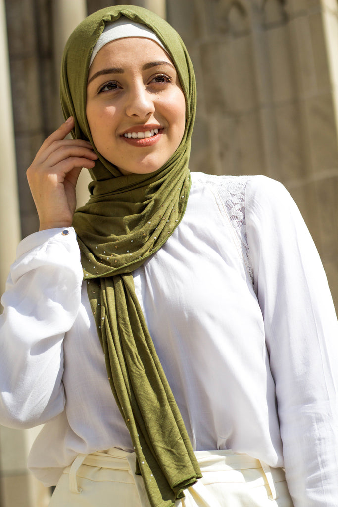 muslim woman wearing white top and pants with a beaded olive green hijab