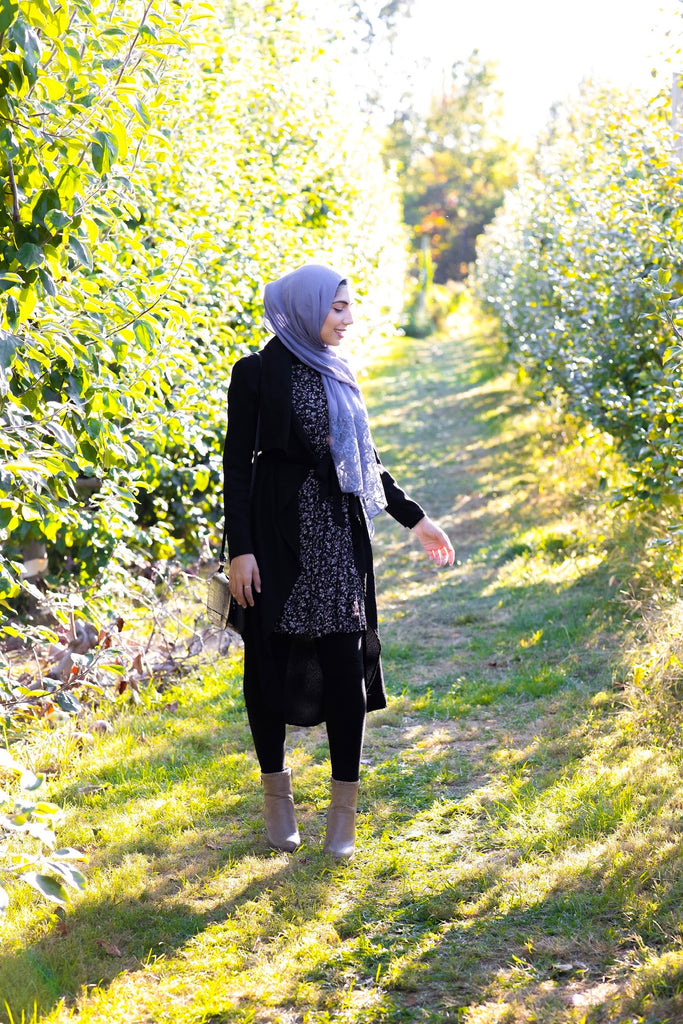 hijabi woman wearing a periwinkle purple modal hijab with lace ends wearing all black in an orchard