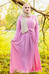 muslim woman wearing a gold shimmer jersey hijab and pink criss cross maxi long sleeve dress with pockets and a waist tie