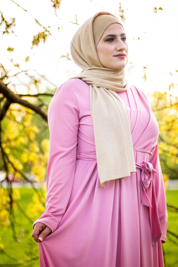 muslim woman wearing a gold shimmer jersey hijab and pink criss cross maxi long sleeve dress with pockets and a waist tie