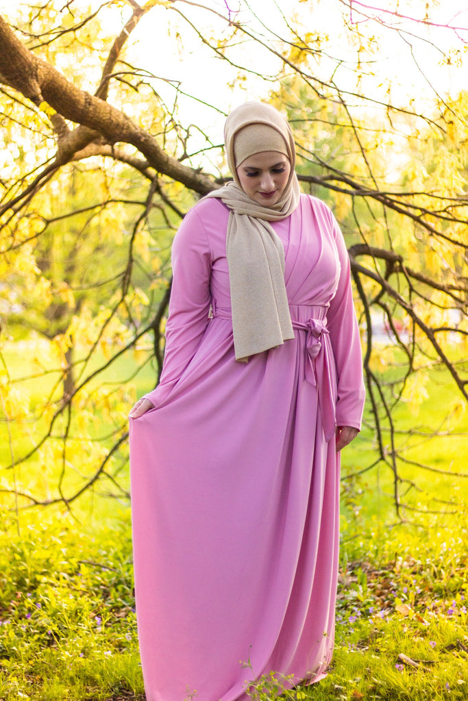 muslim woman wearing a gold shimmer jersey hijab and pink criss cross maxi long sleeve dress with pockets and a waist tie