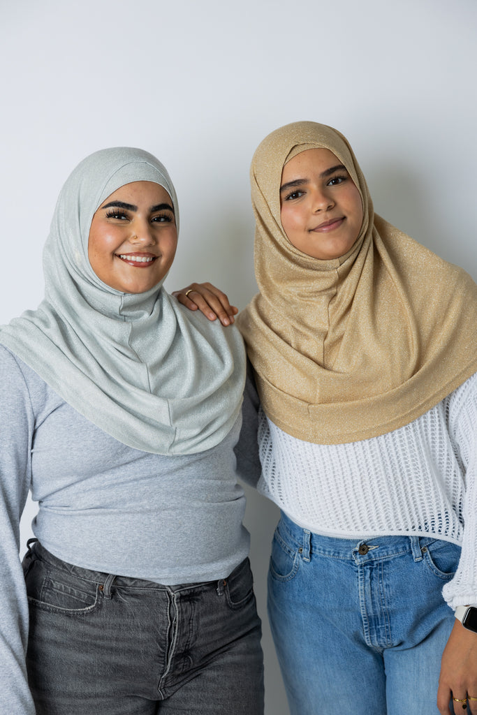 two women wearing a gold shimmer and silver two piece amira slip on hijabs