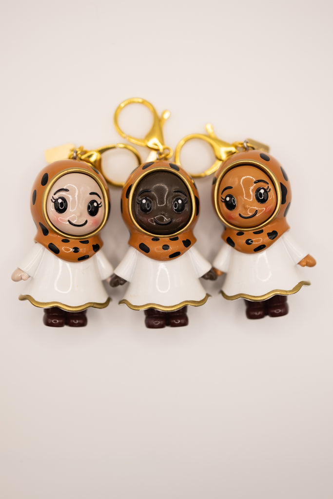 three hijabi figurines in different skin tones in cheetah print hijab on golden keychain