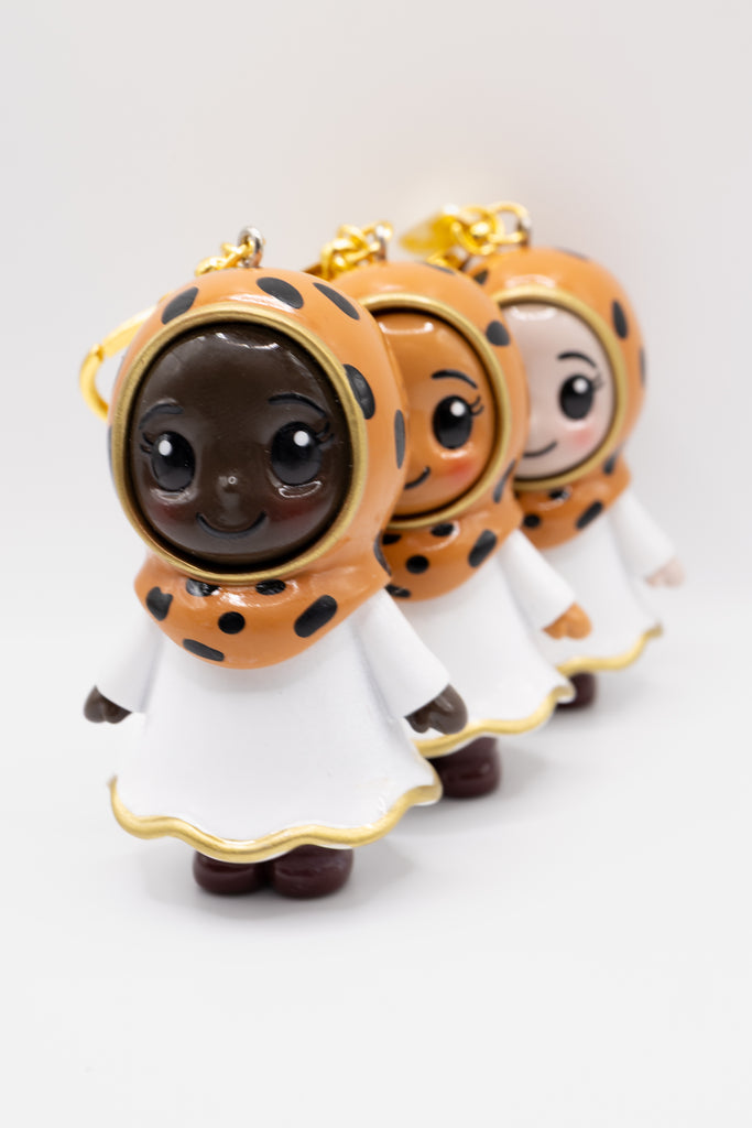 Three hijabi figurines on a keychain with leopard print patterns and white dresses on a light gray background