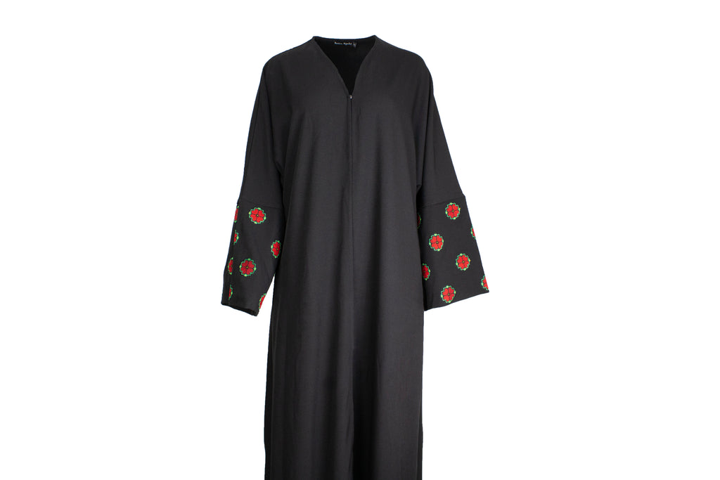 a black abaya with button clasps and pockets and watermelon and poppy tatreez palestinian embroidery along the sleeves 