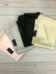 four satin hijabs in light pink, silver, black, and gold on a wooden flatlay