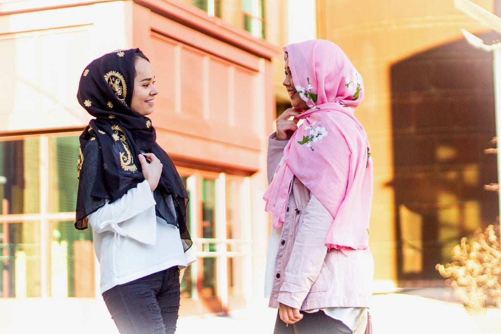 two muslim friends wearing embroidered hijabs in black and gold, and rose and white