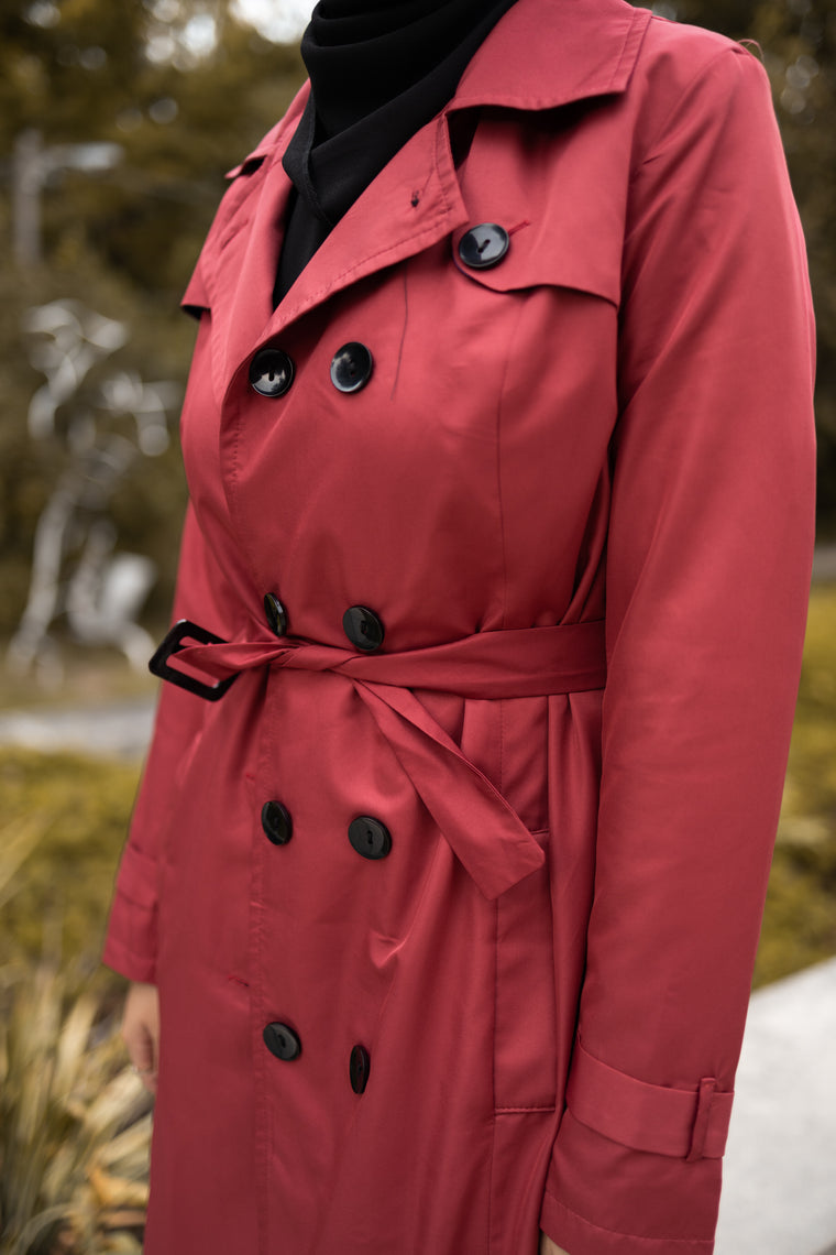 asian muslim woman wearing a black hijab and outfit with a maroon red maxi trench coat with black buttons