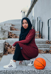 black muslim woman in maroon and black modest workout apparel with a basketball
