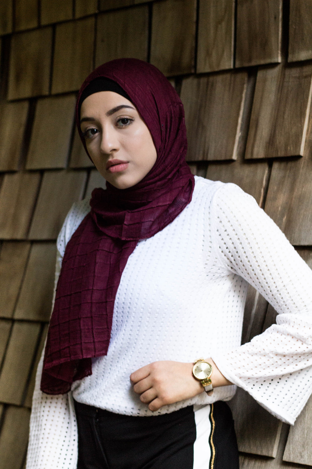 muslim woman wearing a white textured long sleeved top with black pants with a side stripe and a maroon textured grid hijab