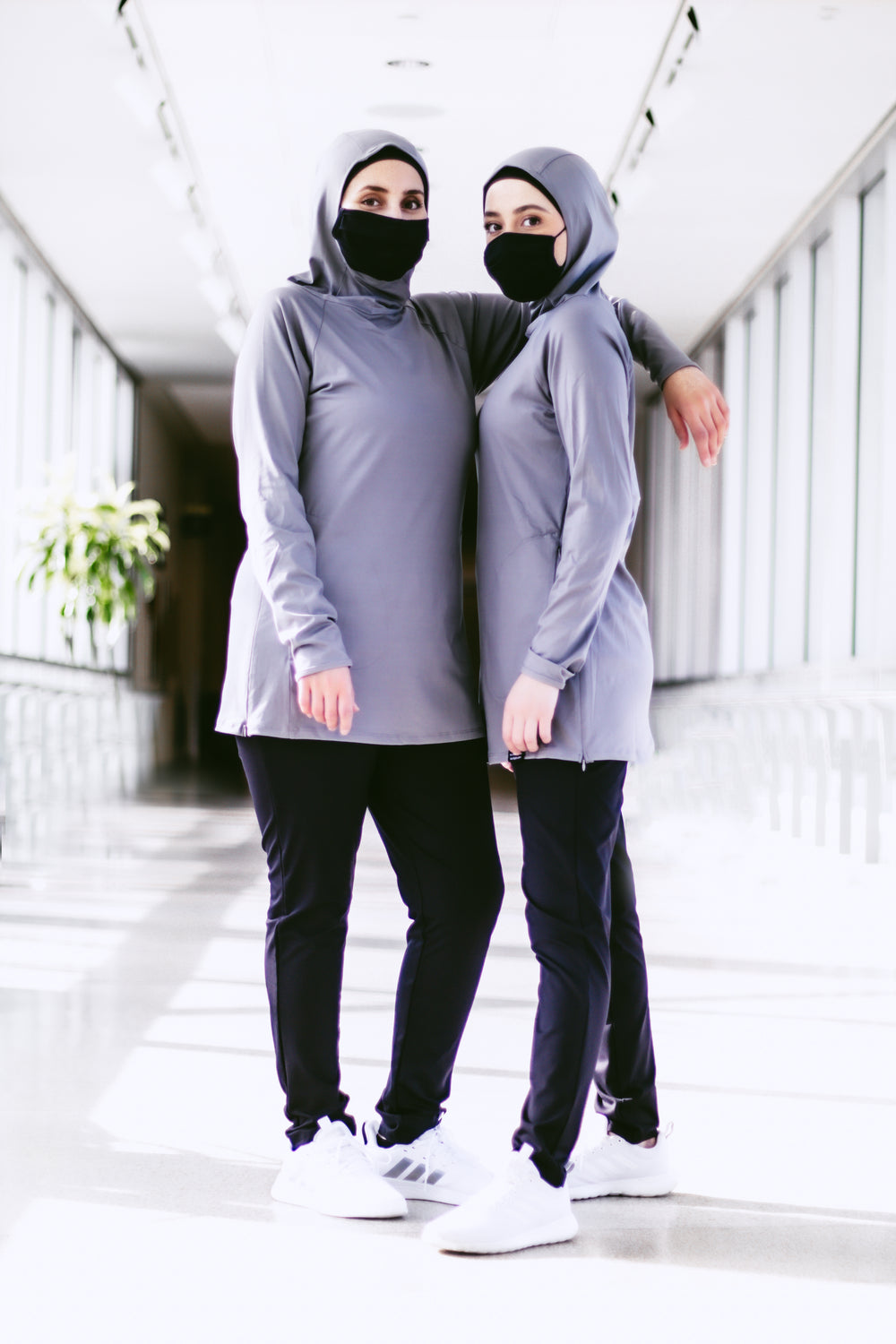 two muslim women in modest workout tops with hijab attached and modest workout pants wearing face masks