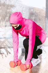 muslim woman lifting red weights and wearing a pink workout top with hijab attached