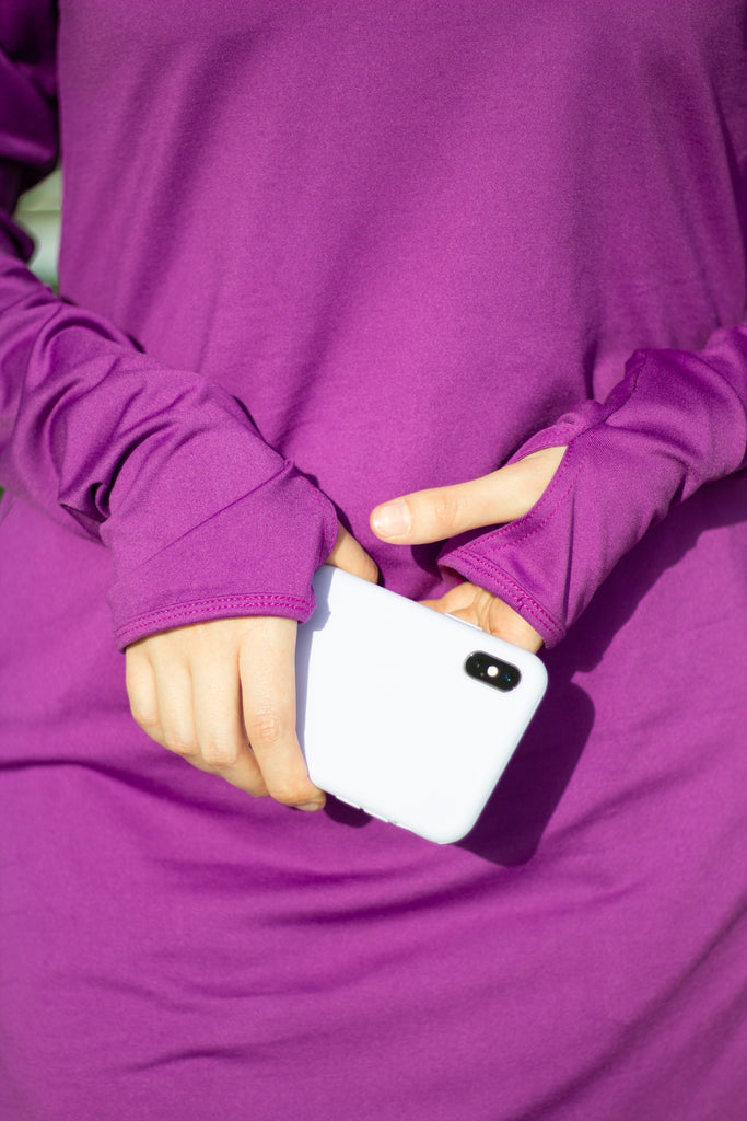 muslim hijabi woman holding an iphone wearing a purple long sleeve workout top
