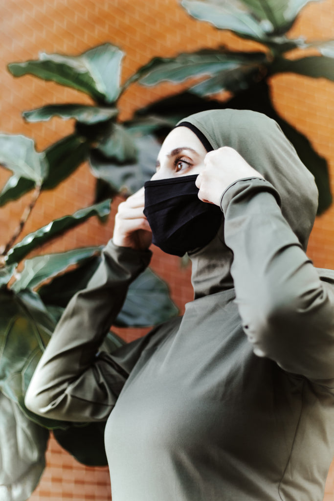 muslim woman adjusting her hijab attached to an olive green workout top