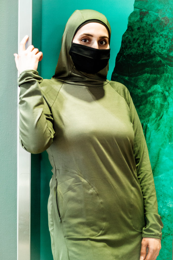 muslim woman posing with covid face mask wearing a long sleeve modest workout top in olive green