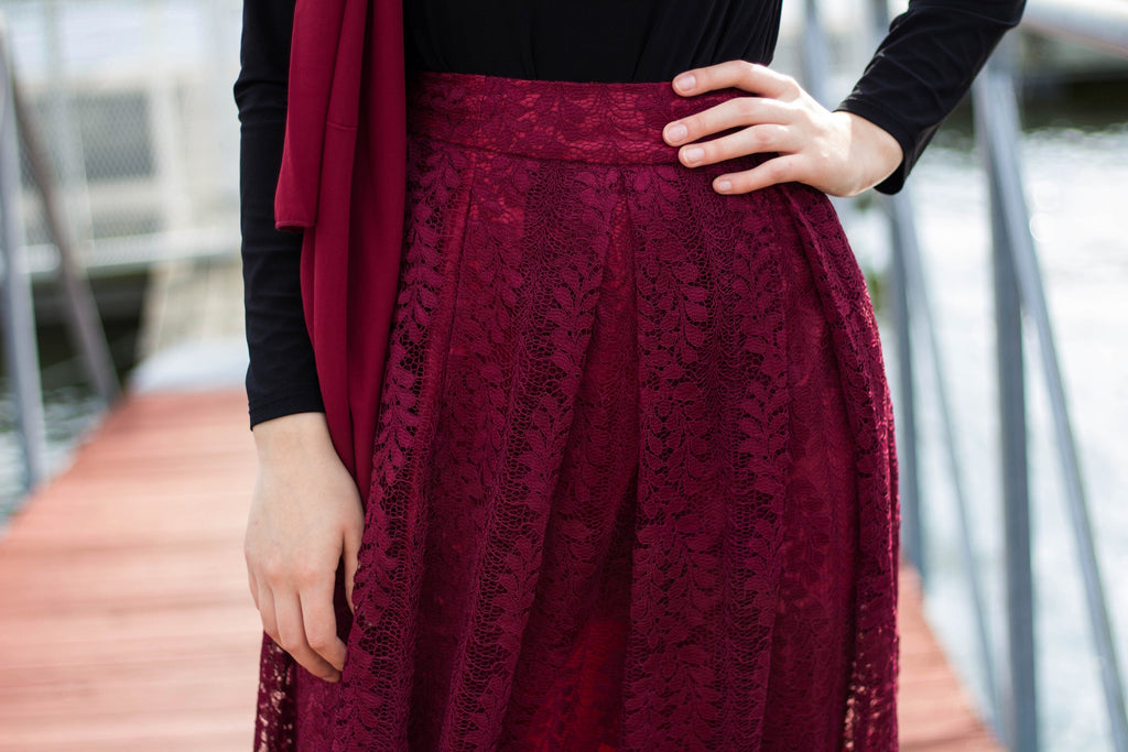 muslim woman wearing a maroon chiffon hijab with a black longsleeved top and maroon lace maxi skirt with pockets