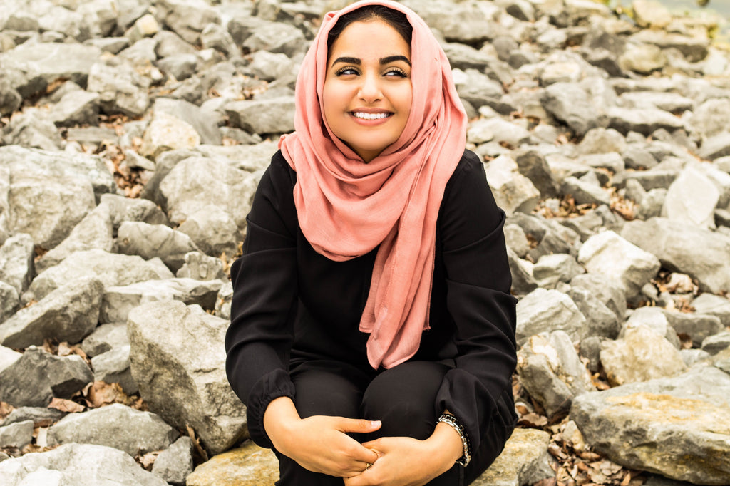 a muslim woman sitting on rocks wearing all black and a mauve bamboo hijab