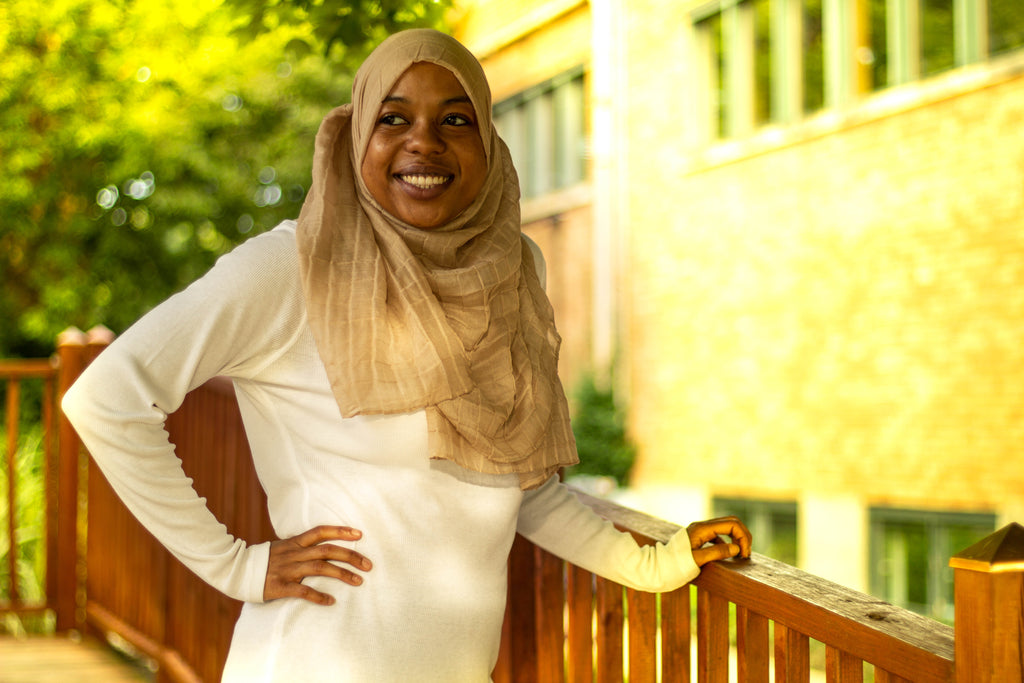 black muslim woman wearing a white long sleeve top and light brown textured hijab