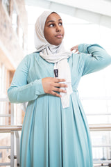 black muslim woman wearing a criss cross teal blue long sleeve elegant maxi dress with a white shimmer jersey hijab