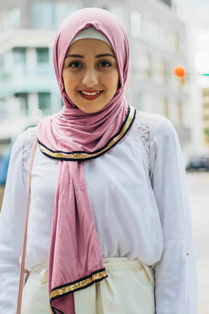 muslim woman wearing white top and white pants with a pink jersey hijab with a gold trim along the edges