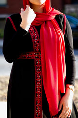 muslim woman in a red chiffon hijab wearing a palestinian embroidered sleeveless kaftan with red embroidery along the edges