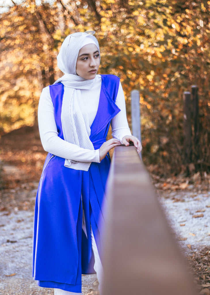 muslim woman wearing a royal blue sleeveless cascade jacket with zipper pockets and a white shimmer jersey hijab
