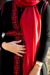 muslim woman in a red chiffon hijab wearing a palestinian embroidered sleeveless kaftan with red embroidery along the edges