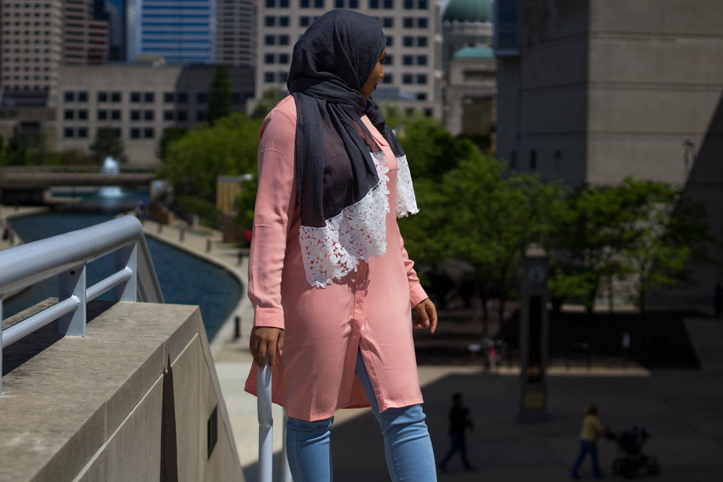 black muslim woman wearing a gray viscose hijab with white embroidered lace and a long sleeved modest blouse in pink