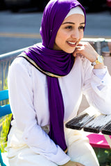 muslim woman wearing white top and white pants and purple jersey hijab with a gold trim