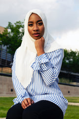 black muslim woman wearing white chiffon square hijab and long sleeve blouse with bow sleeves and blue and white stripes