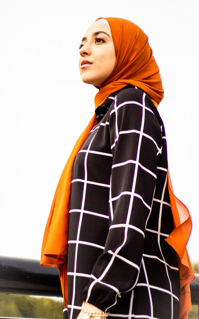 muslim woman wearing black and white grid hijab with burnt orange chiffon hijab 