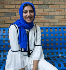 muslim woman with braces wearing all white and a royal blue jersey hijab