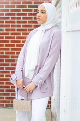 muslim woman wearing a white chiffon hijab and a lilac top with bow sleeves white pants and white heels