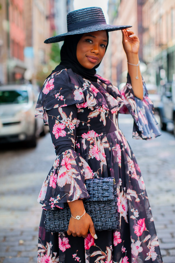 black muslim woman wearing a black hijab and black hat with a floral black and pink dress