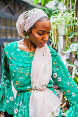 black muslim woman wearing a creme hijab with floral embroidery in white and wearing a green floral dress