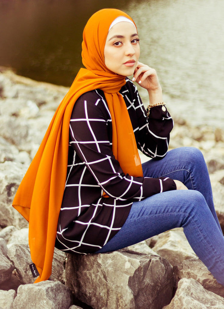 muslim woman wearing black and white grid hijab with burnt orange chiffon hijab and skinny jeans