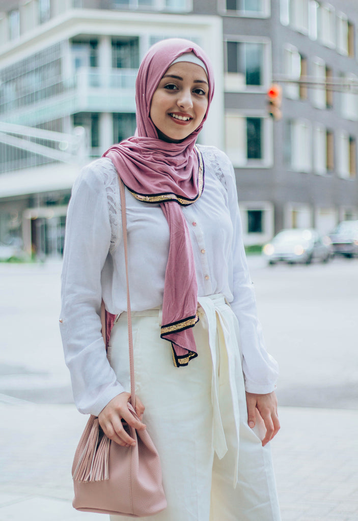muslim woman wearing white top and white pants with a pink jersey hijab with a gold trim along the edges