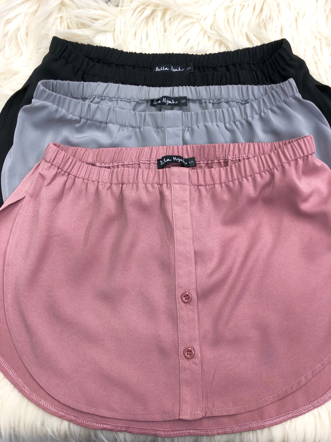 bundle of fake shirt extenders in black, gray, and mauve with buttons and an elastic waistband