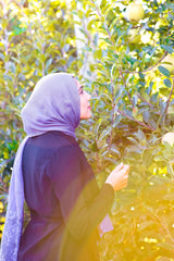 hijabi woman wearing a periwinkle purple modal hijab with lace ends wearing all black in an orchard