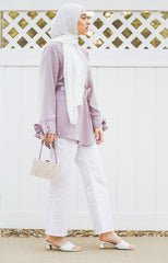 muslim woman wearing a white chiffon hijab and a lilac top with bow sleeves white pants and white heels