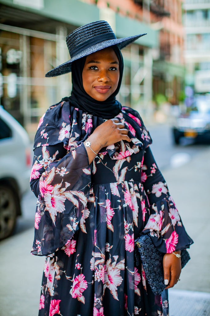black muslim woman wearing a black hijab and black hat with a floral black and pink dress