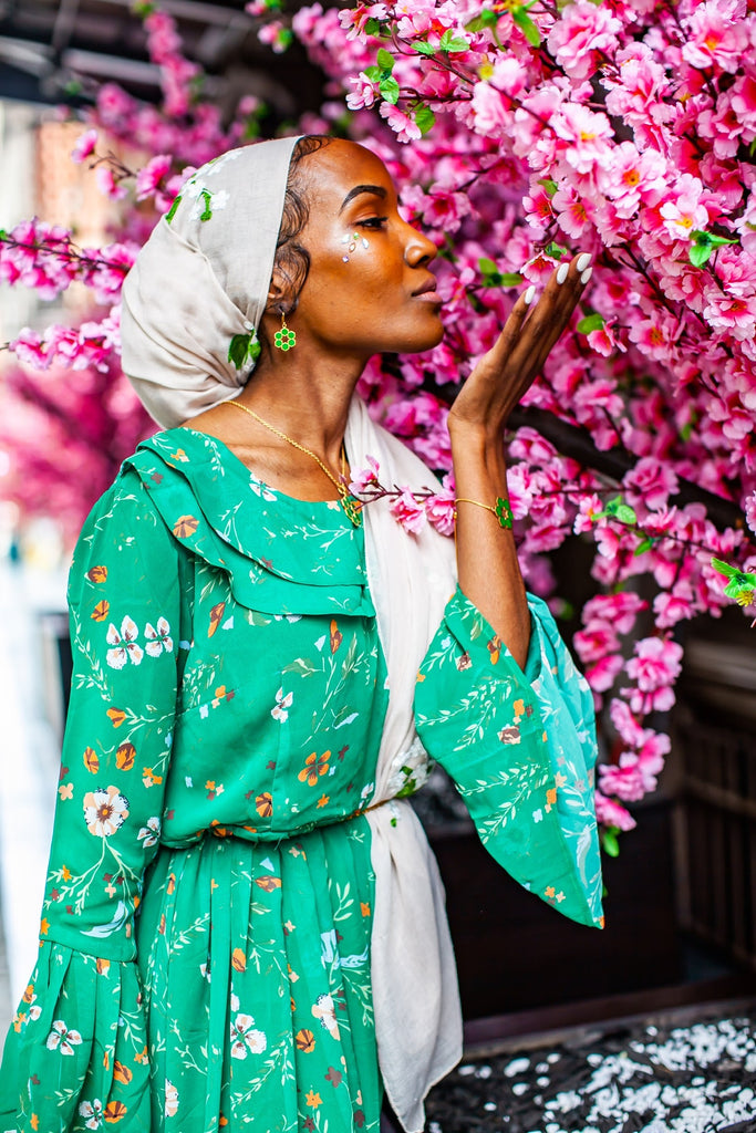 black muslim woman wearing a creme hijab with floral embroidery in white and wearing a green floral dress
